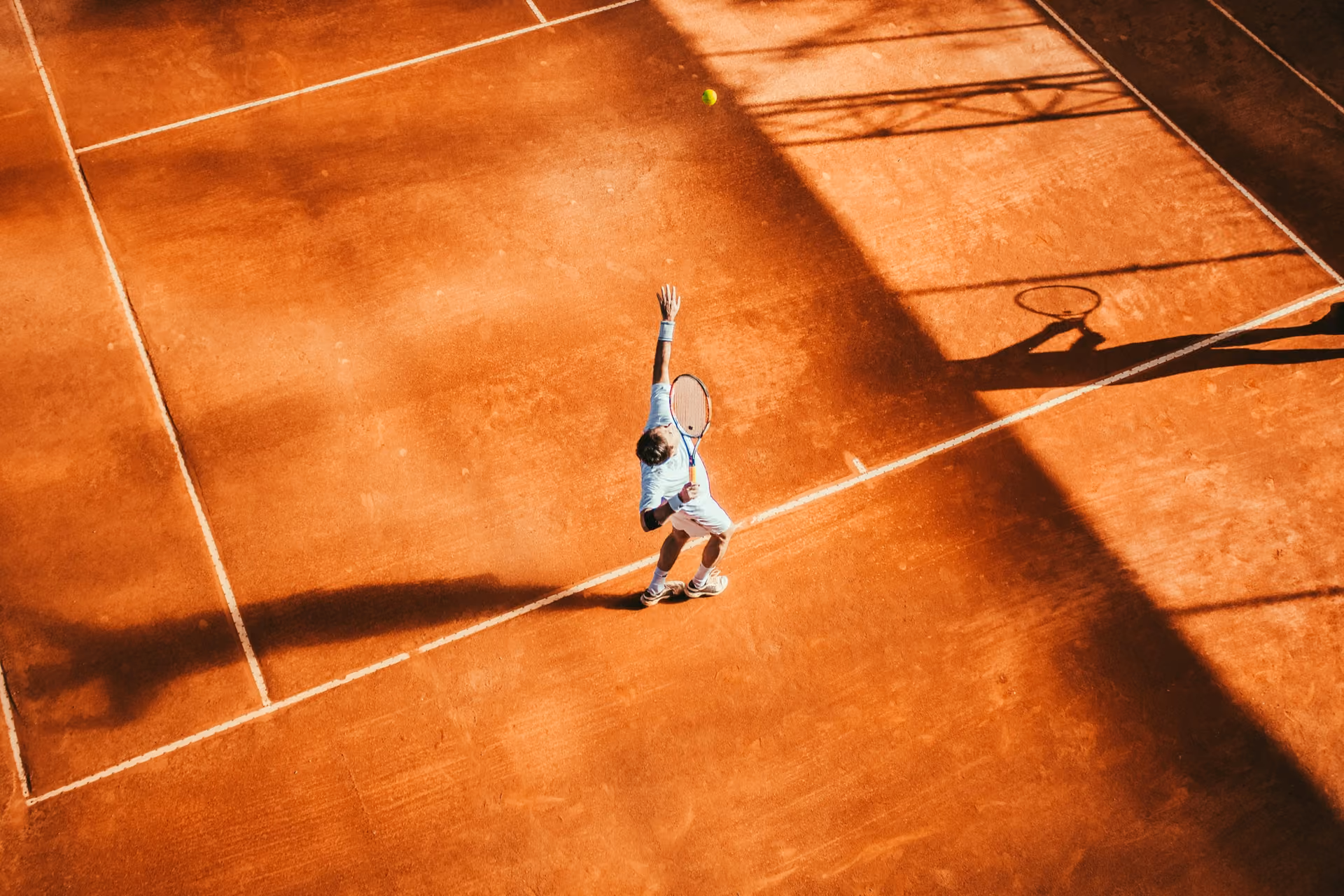 Joueur de tennis au service sur un court en terre battue, vu du ciel