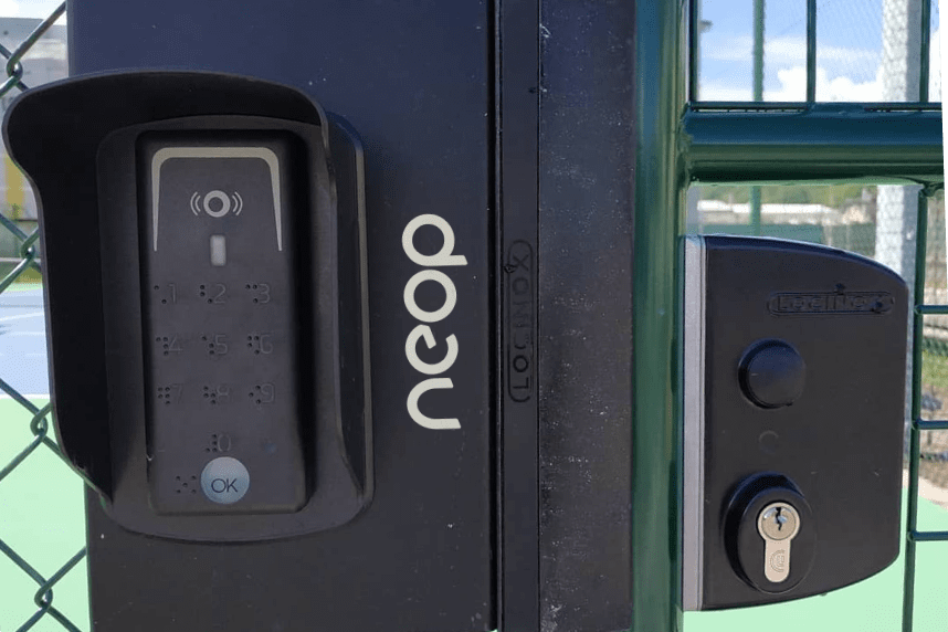 Lecteur à codes Neop sous sa protection et serrure de portillon sur un court de tennis