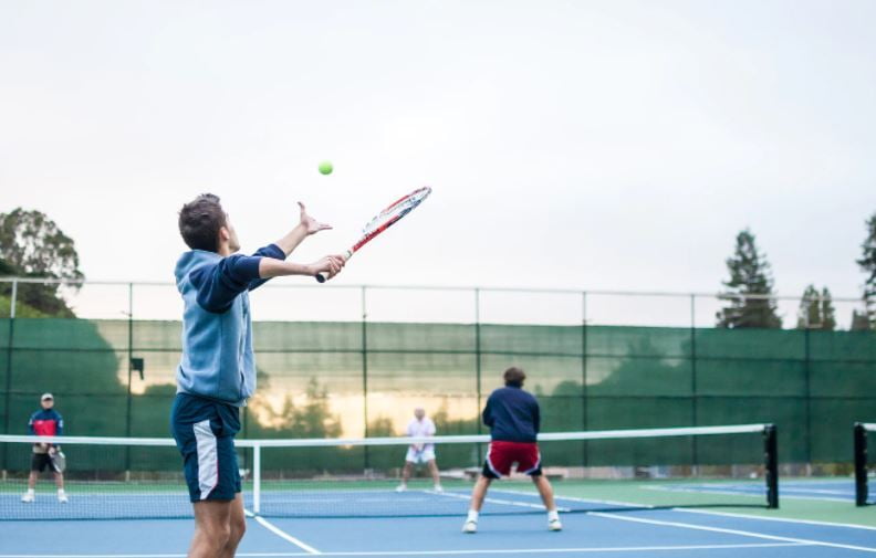 Joueur au service lors d’une partie de double sur un court de tennis extérieur