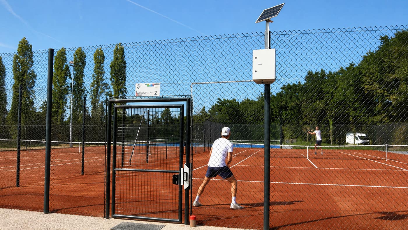 Portillon d’un court de tennis en terre battue équipé d’une serrure connectée Neop, avec boîtier de contrôle d’accès alimenté par panneau solaire